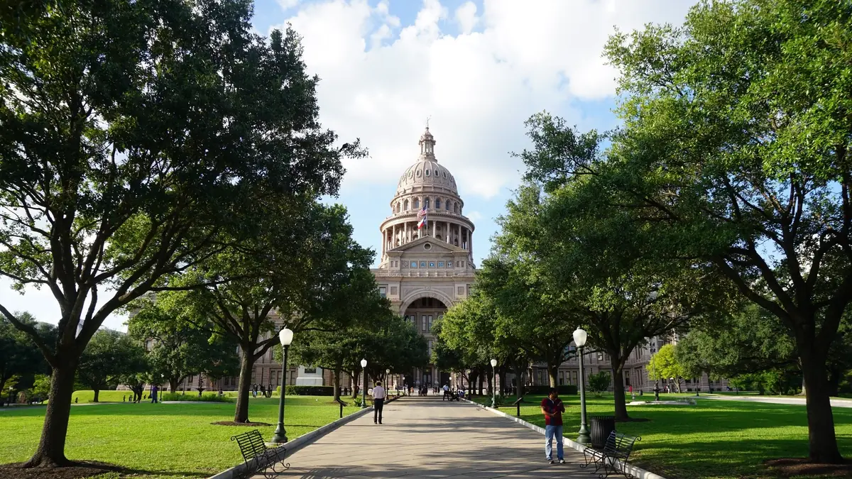 The Texas State Capitol in Austin seen down a tree-lined walkway on the Capitol grounds